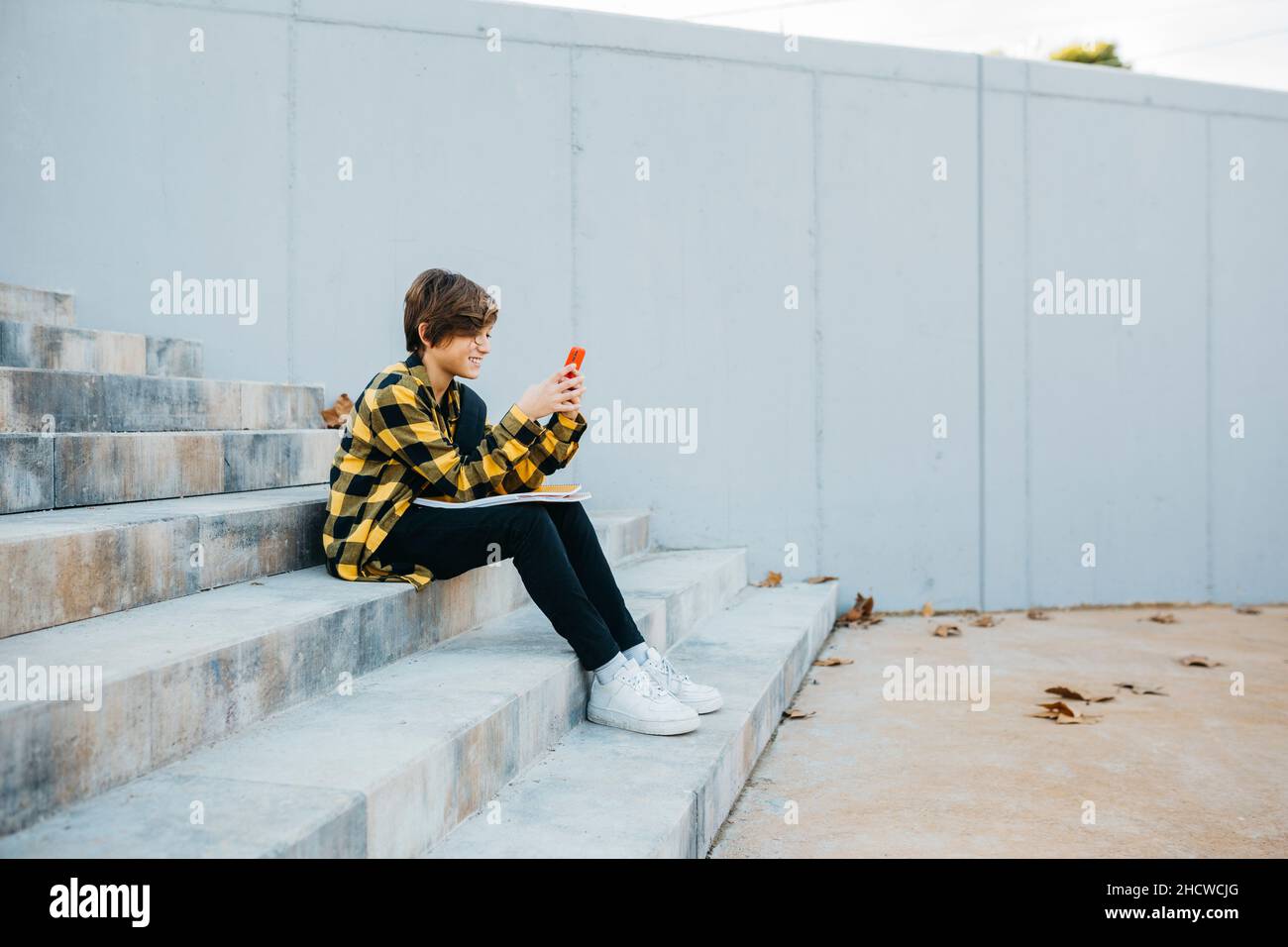 Teen student using a red smartphone and sitting on stairs outdoors Stock Photo