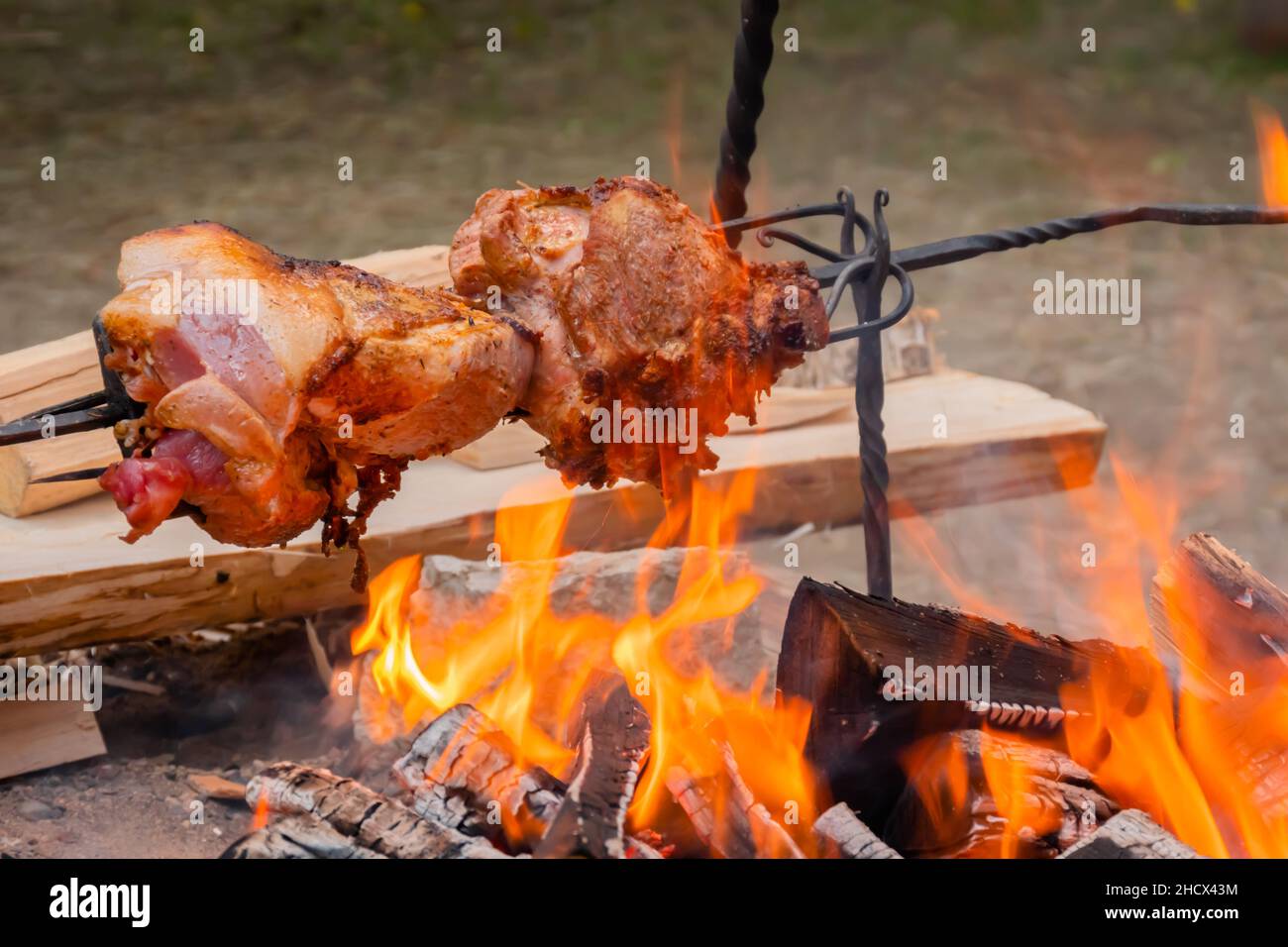 Process of cooking large meat peaces on spit over open fire Stock Photo
