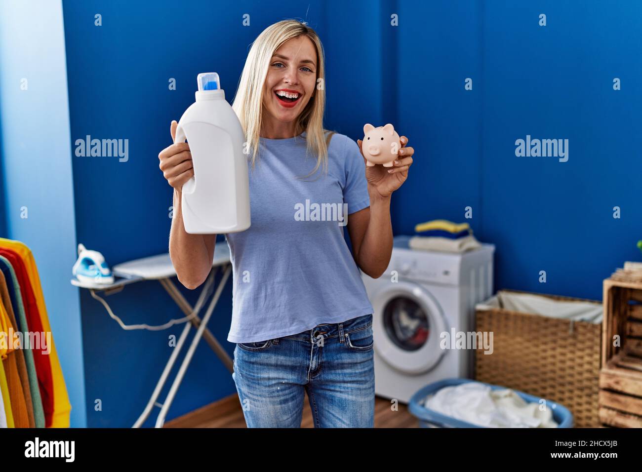 Beautiful woman doing laundry holding detergent bottle and piggy bank