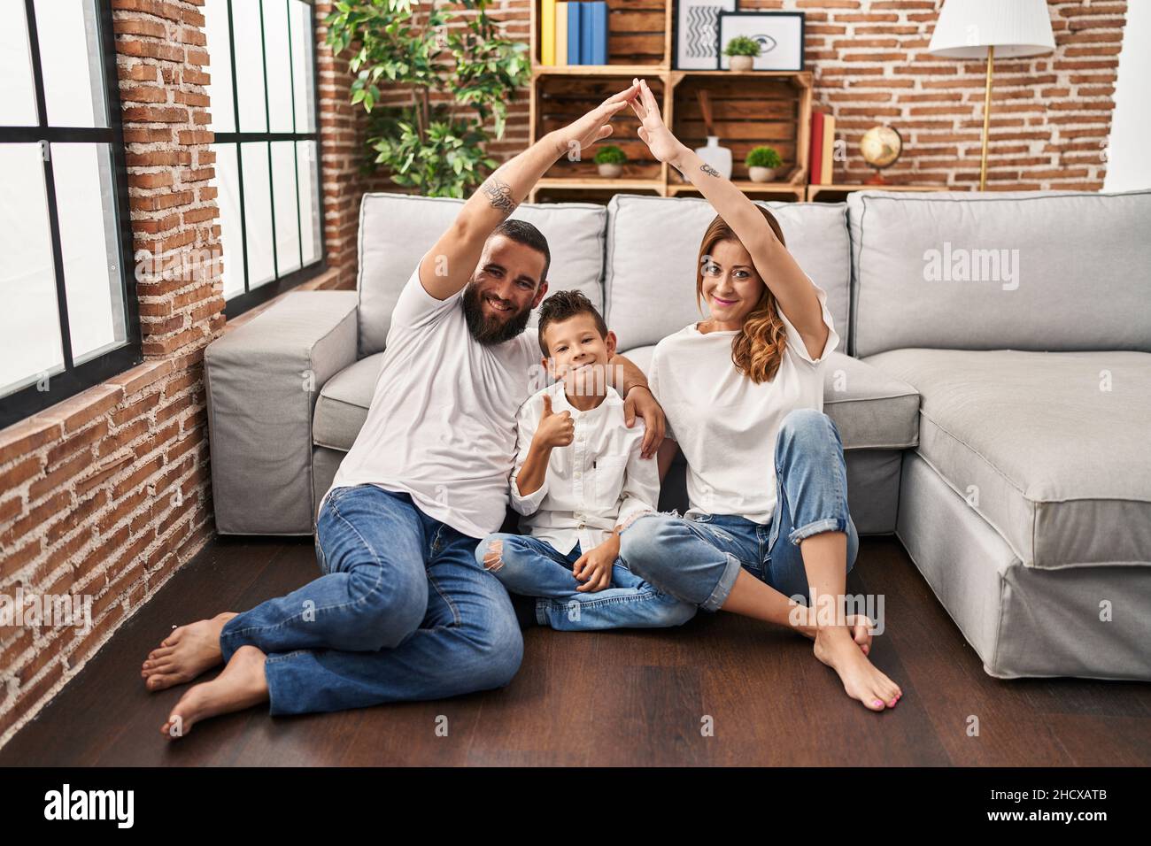 Family of three doing house shape with arms smiling happy and positive, thumb up doing excellent and approval sign Stock Photo