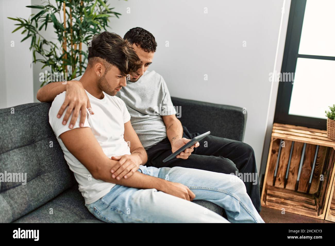 Two hispanic men couple using touchpad hugging each other at home Stock ...