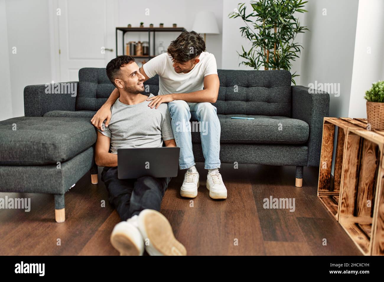 Two hispanic men couple using laptop hugging each other at home Stock ...