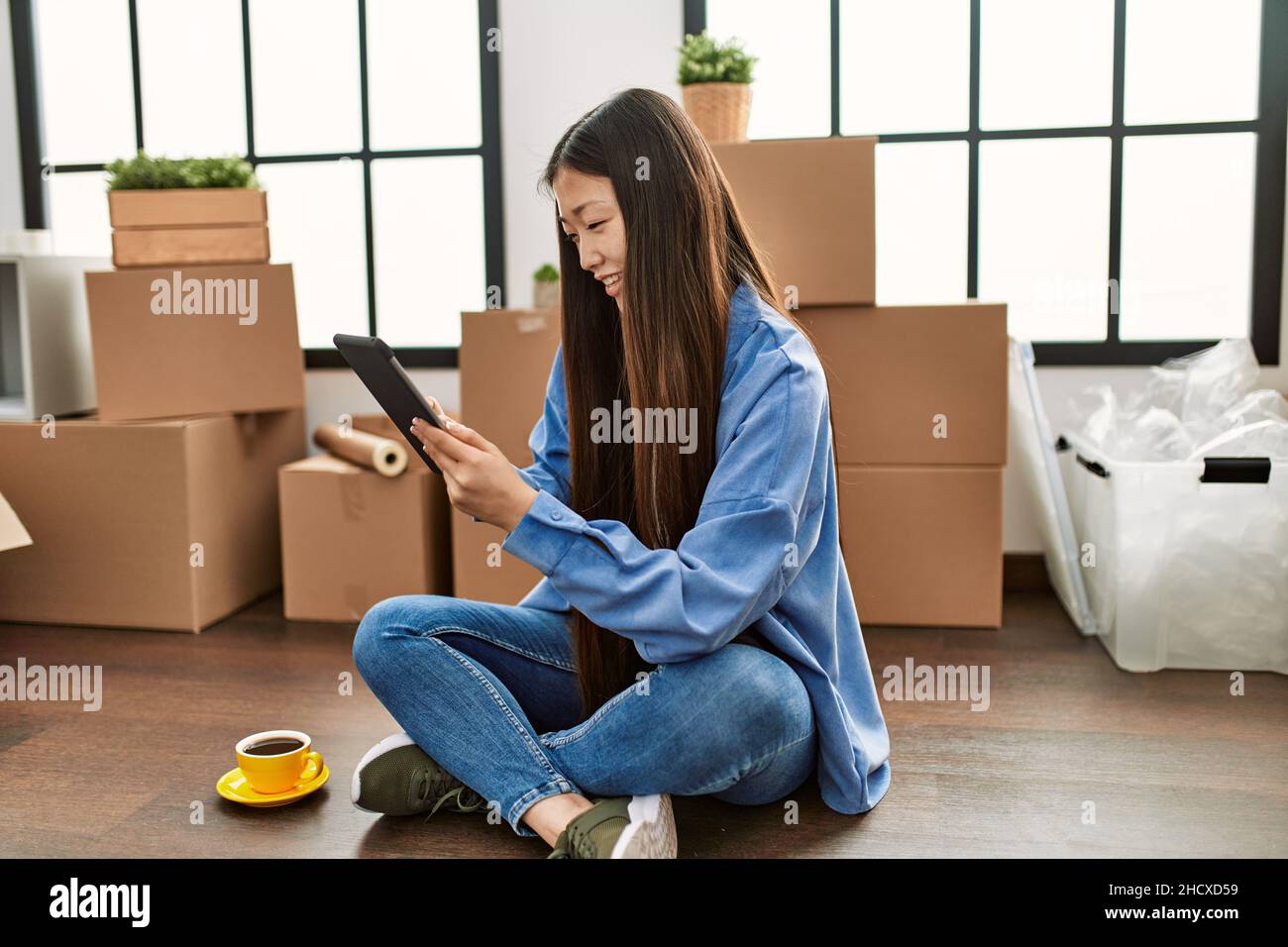 Young chinese girl smiling happy using touchpad sitting on the floor at ...