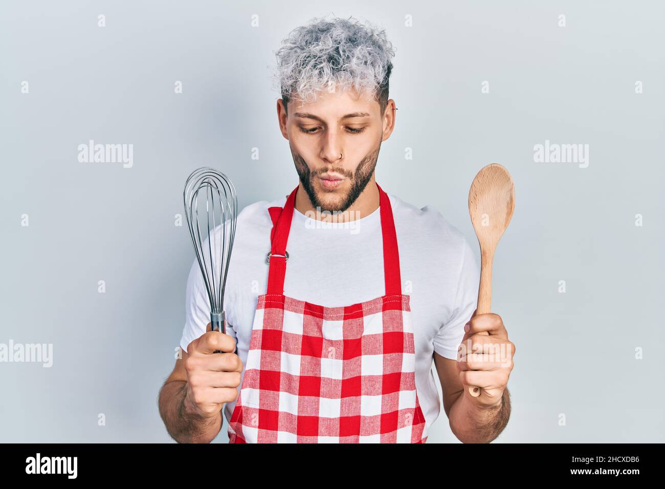 Young hispanic man with modern dyed hair wearing cook apron holding