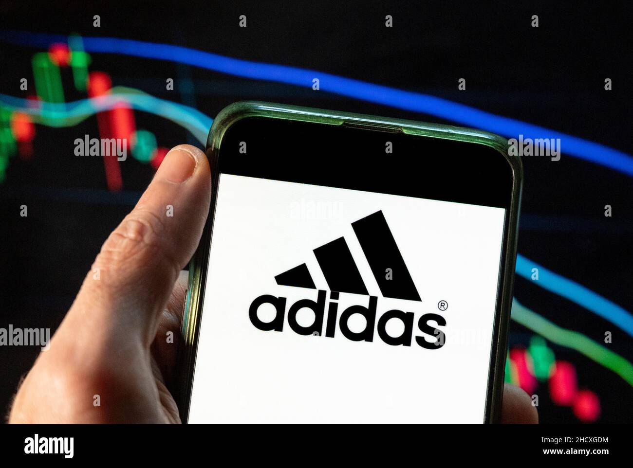 In this photo illustration the German multinational sport clothing brand  Adidas logo seen displayed on a smartphone with an economic stock exchange  index graph in the background Stock Photo - Alamy