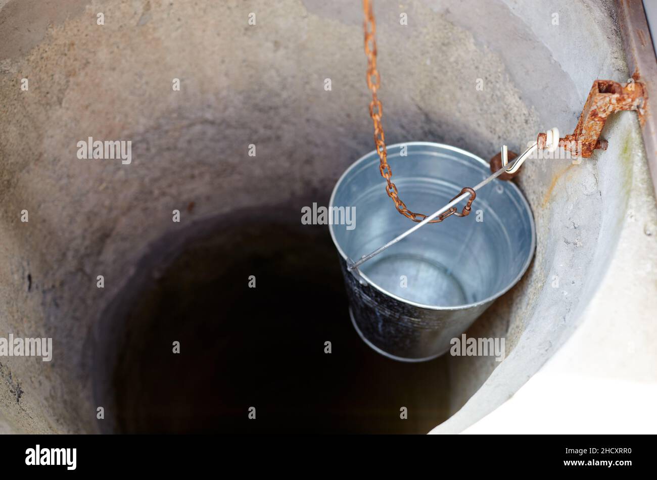 Metal bucket in drawwell in European village. Retro stone water well in rural area Stock Photo