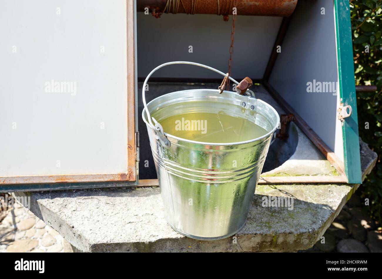Metal bucket at draw-well in European village. Retro stone water well in rural area Stock Photo