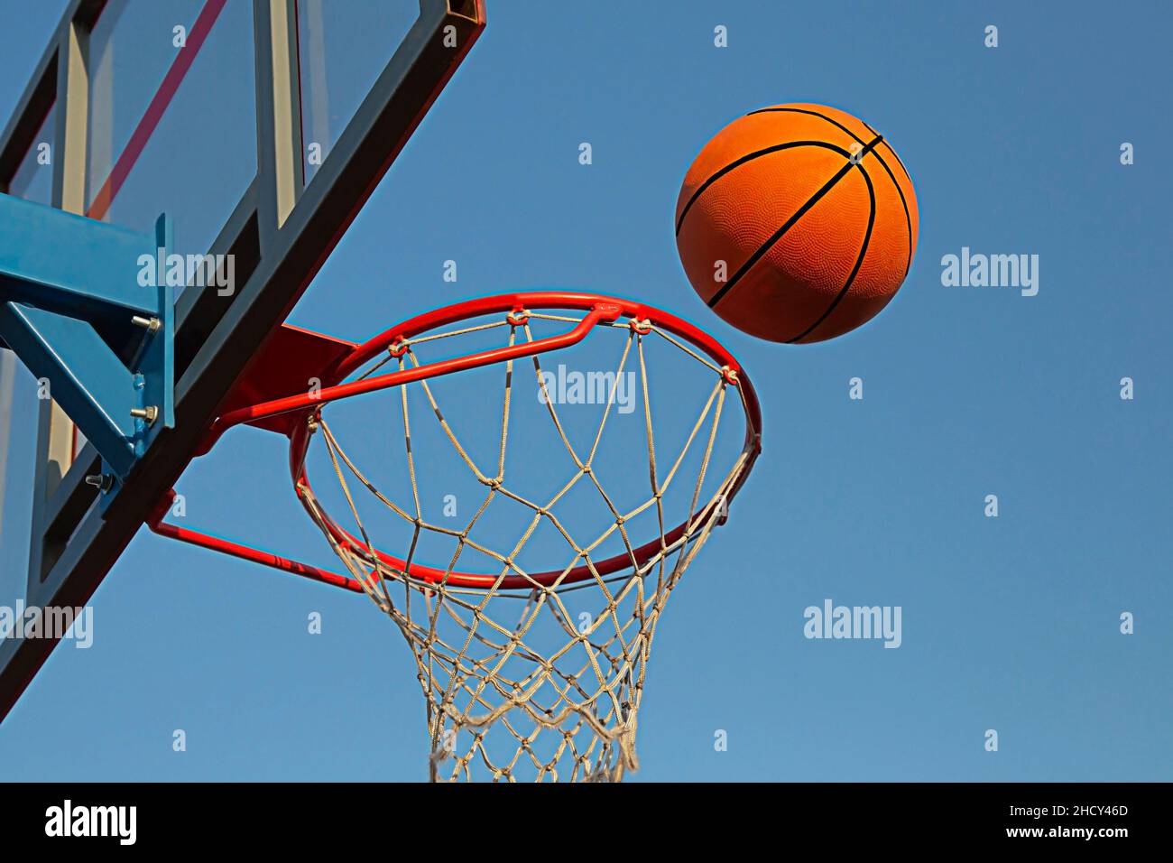 A basketball in a net on a blue sky background. The ball hit the ring. Sports, team game. Conceptual: victory, success, hitting the target, sport. Stock Photo