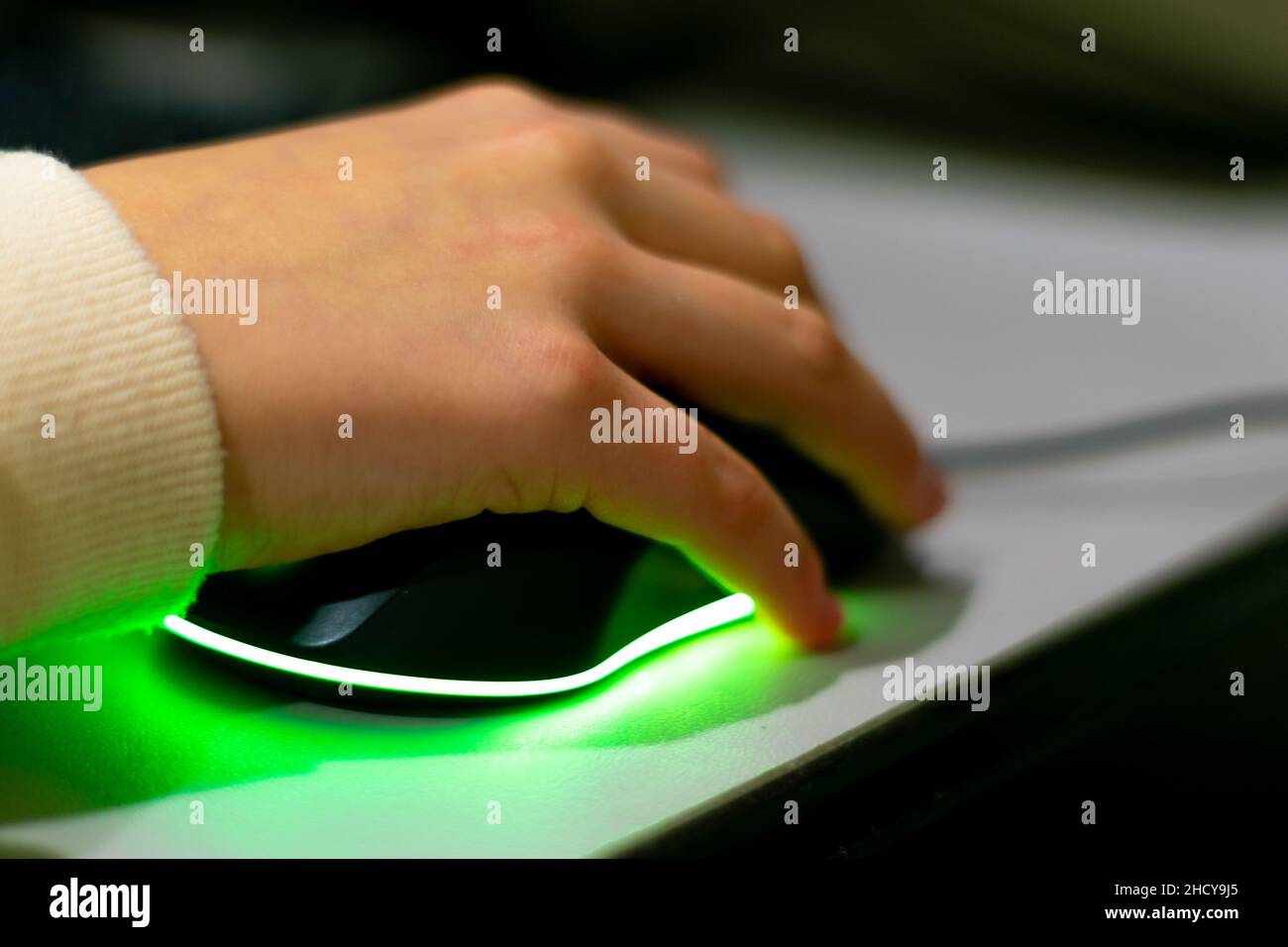 Kids playing computer games, hand holding gaming colorful mouse with green light. Stock Photo
