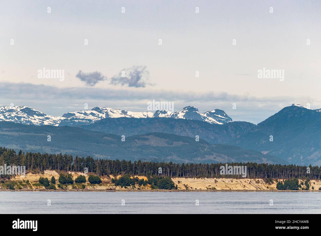 A view from the Strait of Georgia of Denman Island's ecologically sensitive Komas Bluffs, with Vancouver Island's Comox Glacier in the background. Stock Photo