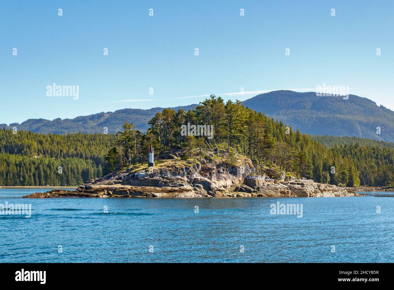 Summer sea level view of an islet with a navigation marker (at Greene Point Rapids in Cordero Channel on British Columbia's Inside Passage). Stock Photo