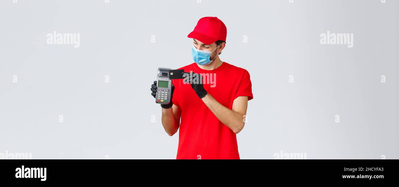 Contactless delivery, payment and online shopping during covid-19, self-quarantine. Courier in red uniform and gloves with face mask, showing POS payi Stock Photo
