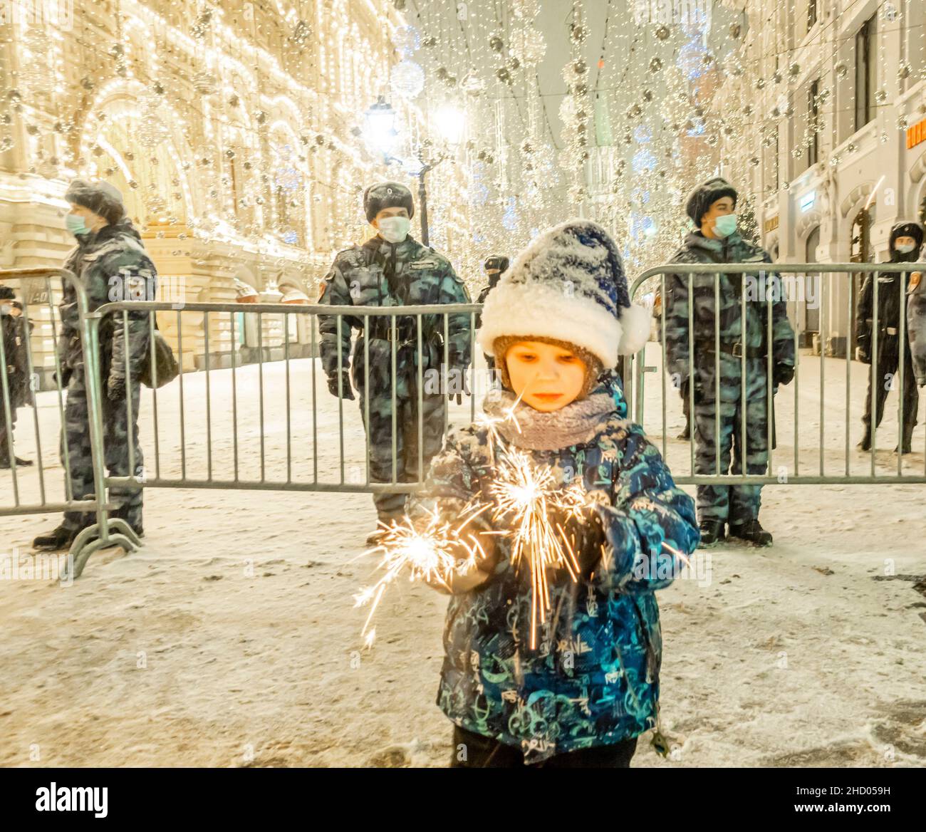 A kid child with lit up sparklers standing in front of the guarded entrance with Rosgvardia policemen on a New-Year night, central Moscow, Russia Stock Photo
