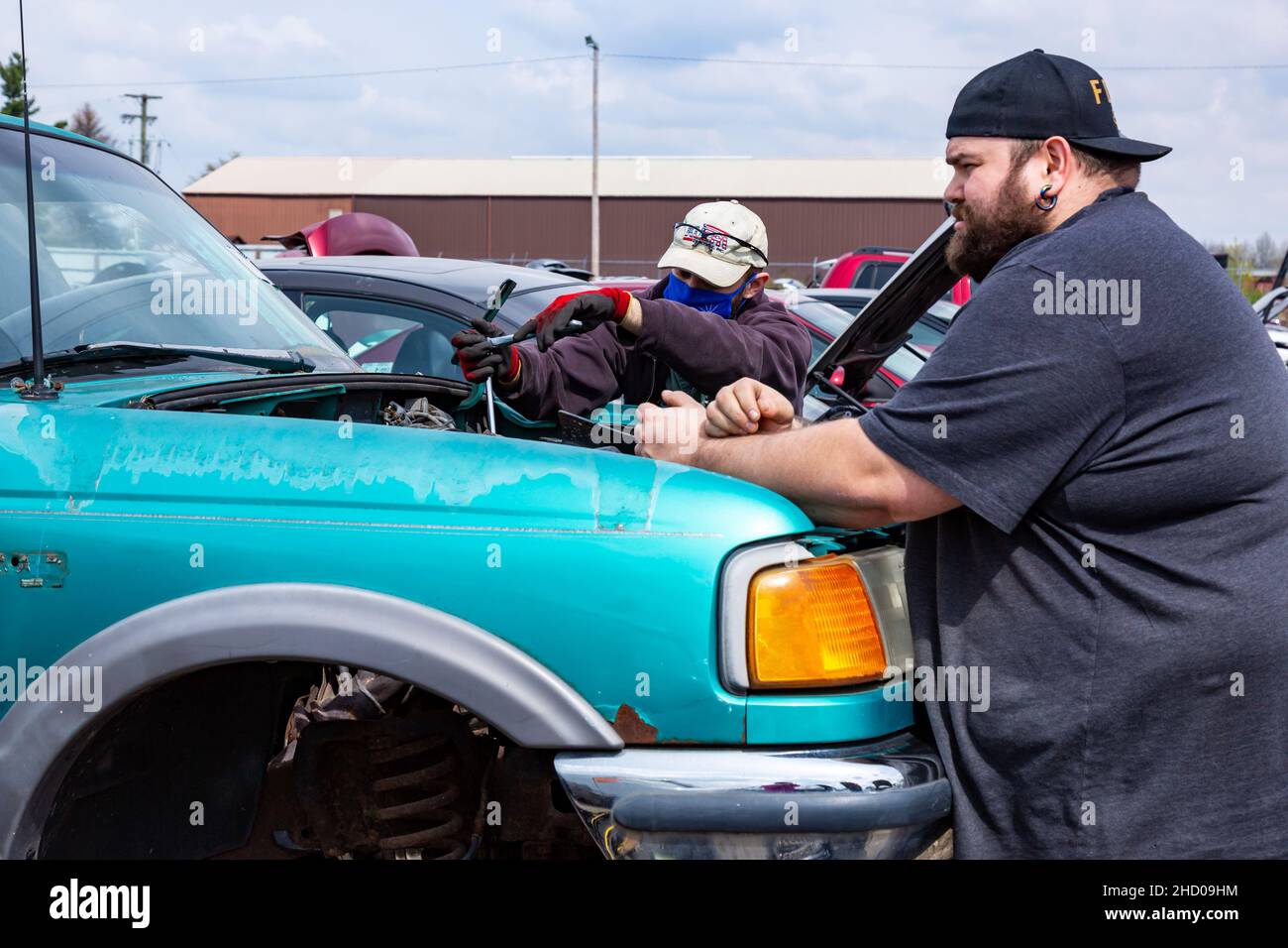 Two men work to remove parts from a blue Ford Ranger pickup truck at the LKQ Pick Your Part auto salvage yard in Fort Wayne, Indiana, USA. Stock Photo