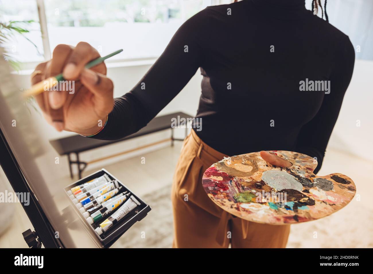 Imaginative young artist painting on a canvas. Unrecognizable female painter holding a palette while drawing in her art studio. Creative young freelan Stock Photo