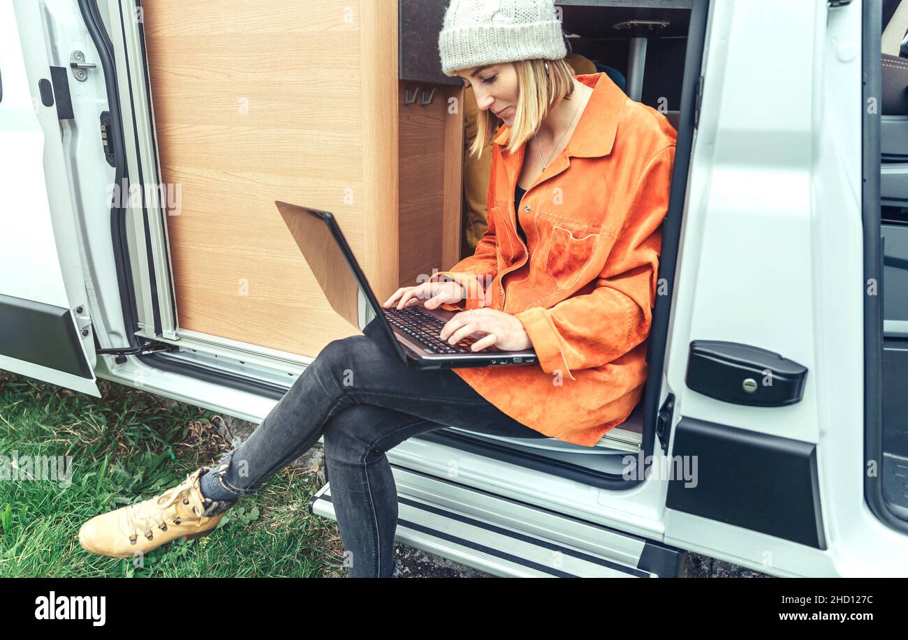 Woman teleworking sitting in the door of campervan Stock Photo