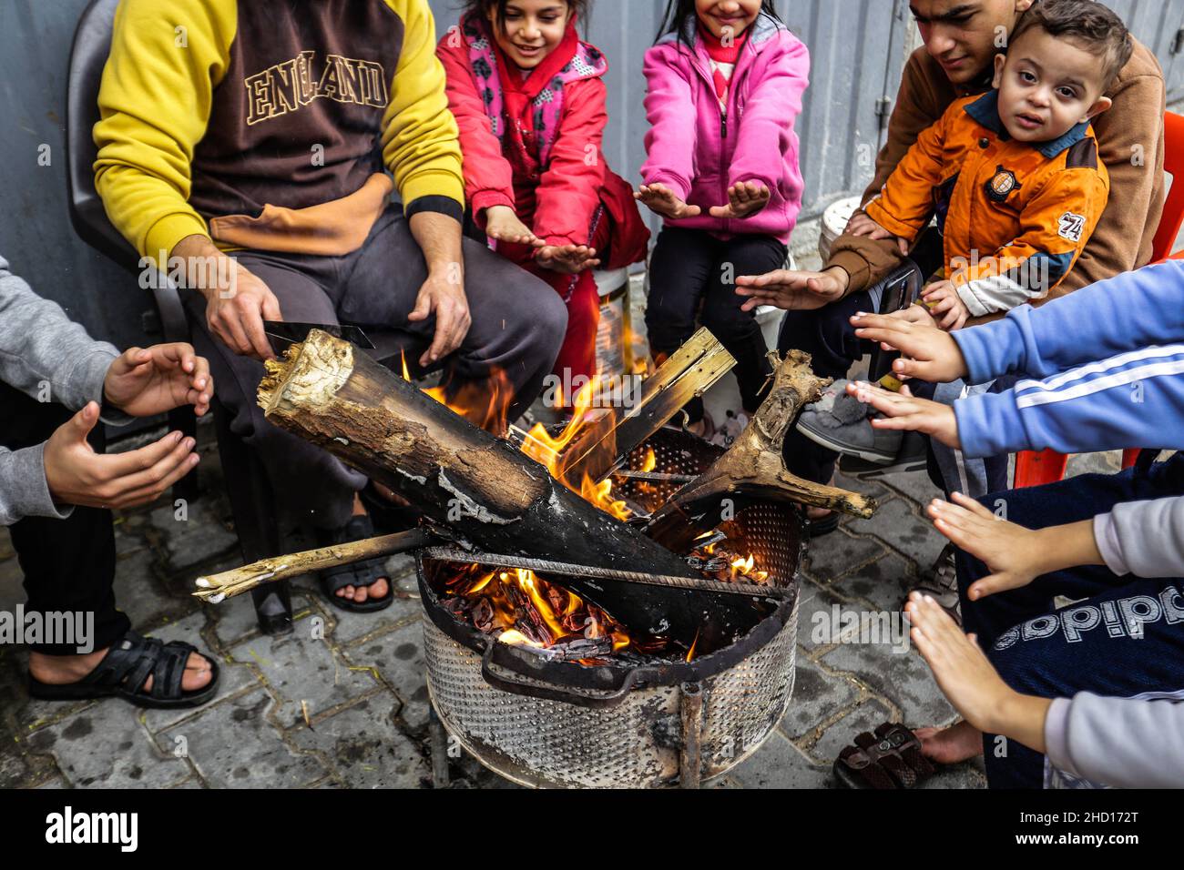 Palestinian refugees warm themselves around a fire in a poor ...