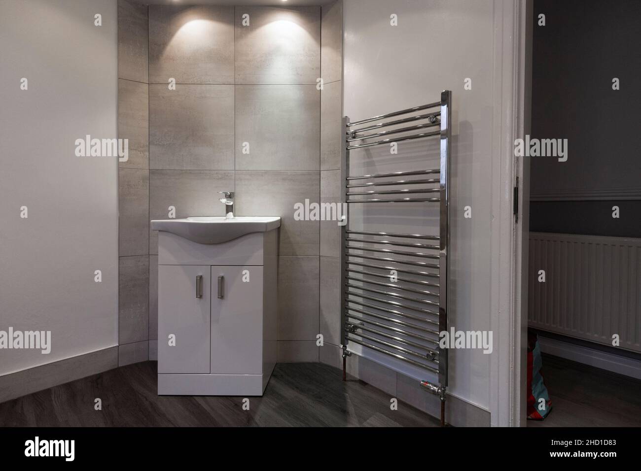 Modern bathroom with vanity unit, large Barrington  white tiles, LVT vinyl flooring grey and white walls, large towel rail, spot lights Stock Photo