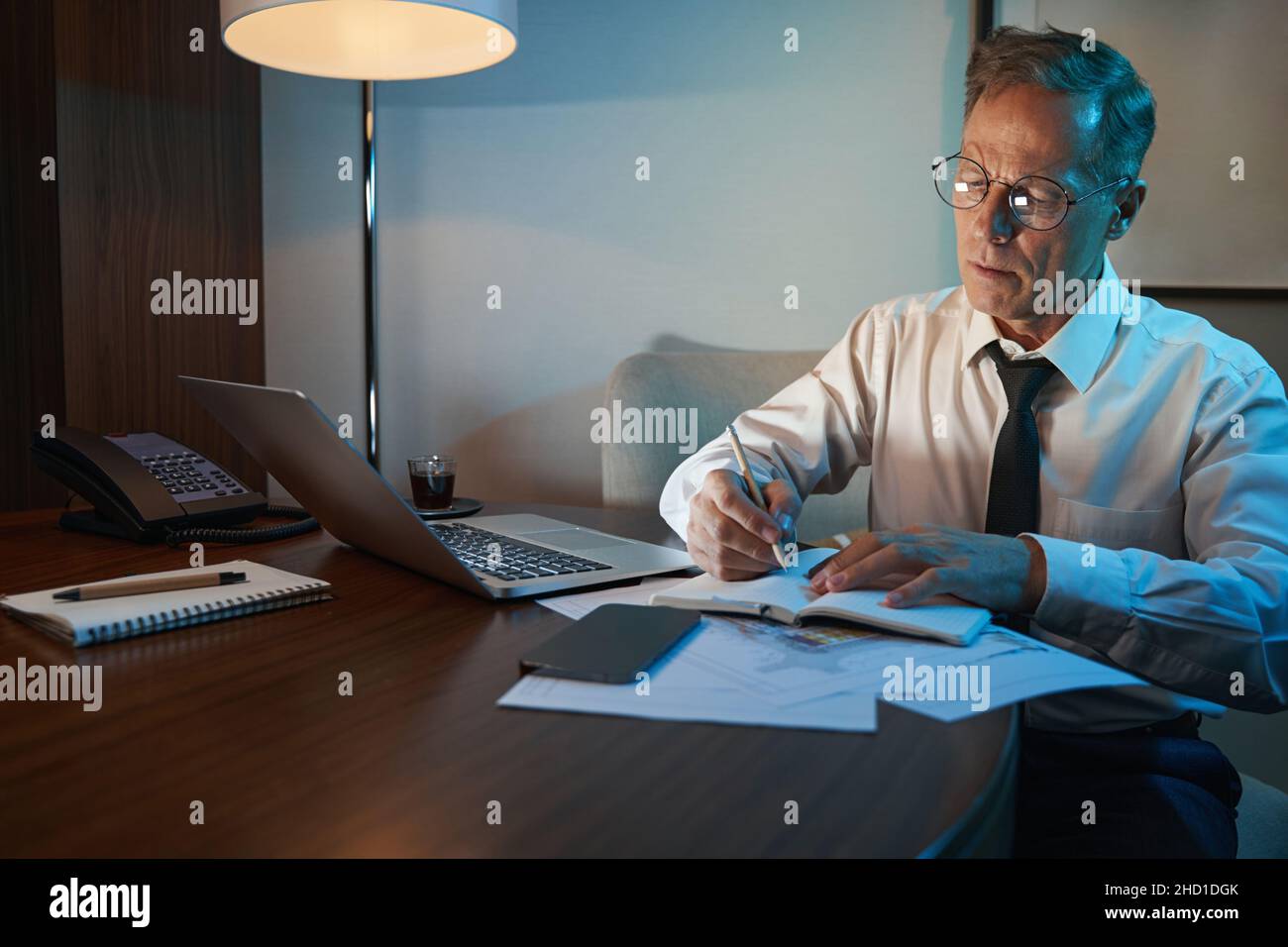 Mature businessman working overtime in dimly lit hotel room Stock Photo -  Alamy