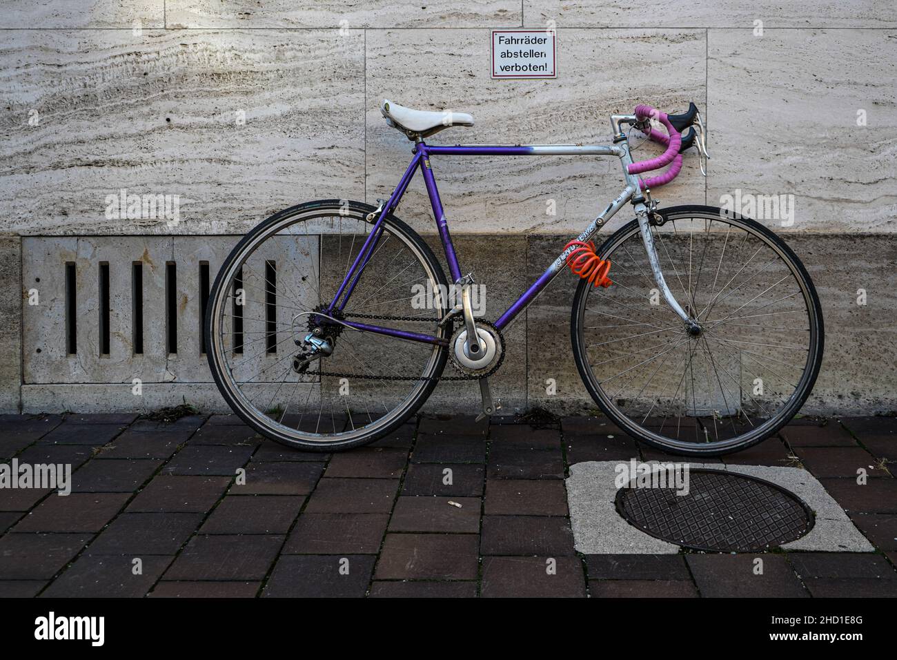 A purple Bicycle parked against a wall with a sign Bikes not allowed to park. Stock Photo