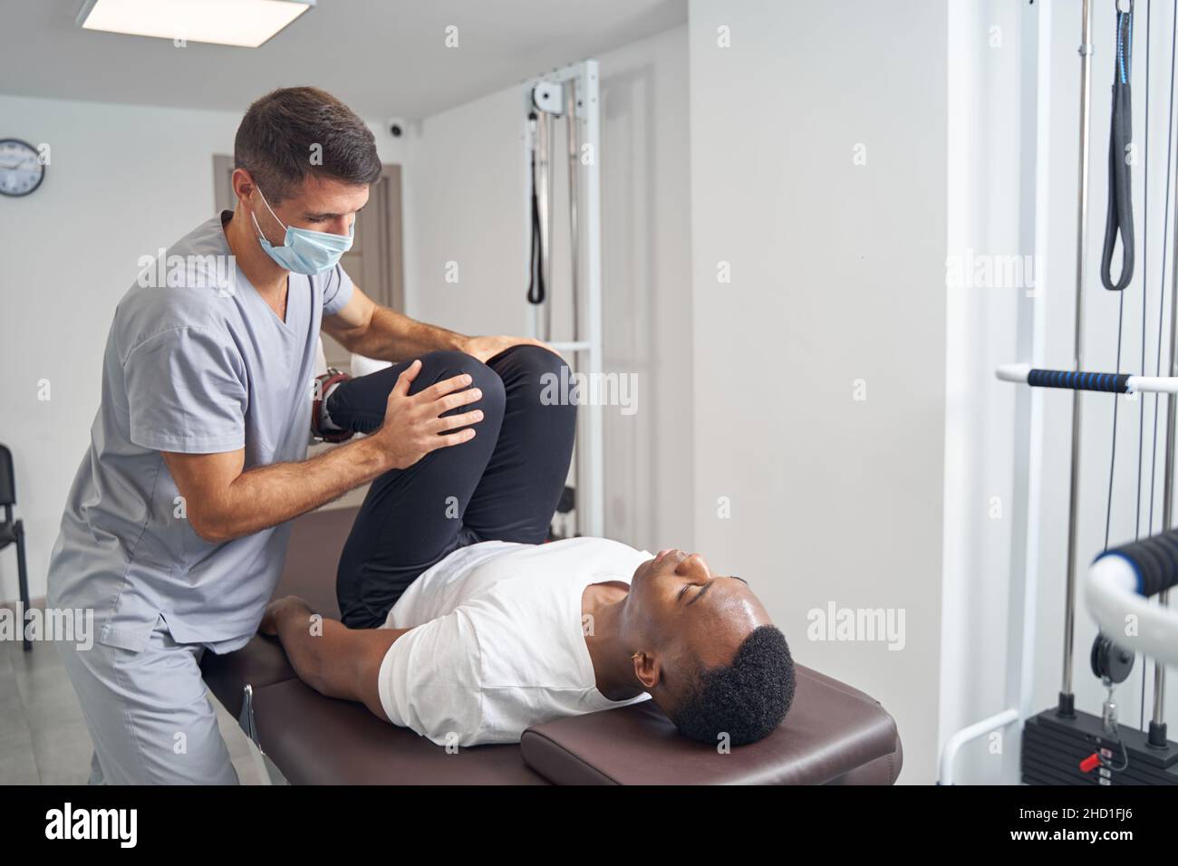 Doctor in protective mask stretching patient leg muscles Stock Photo