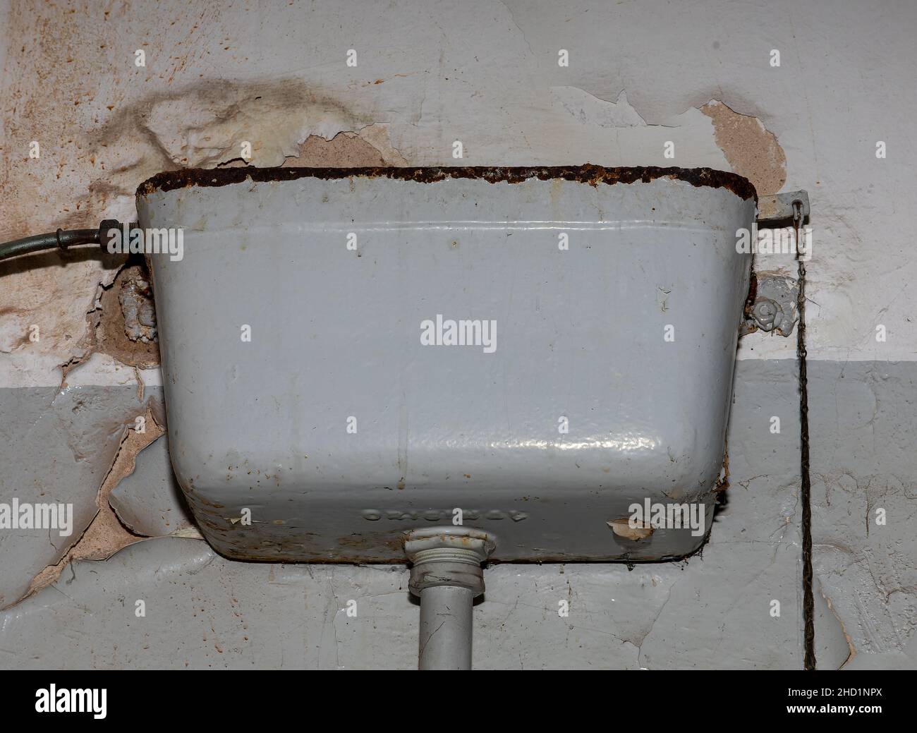 old, rusted cistern above the toilet with chipped plaster in a house in need of renovation Stock Photo