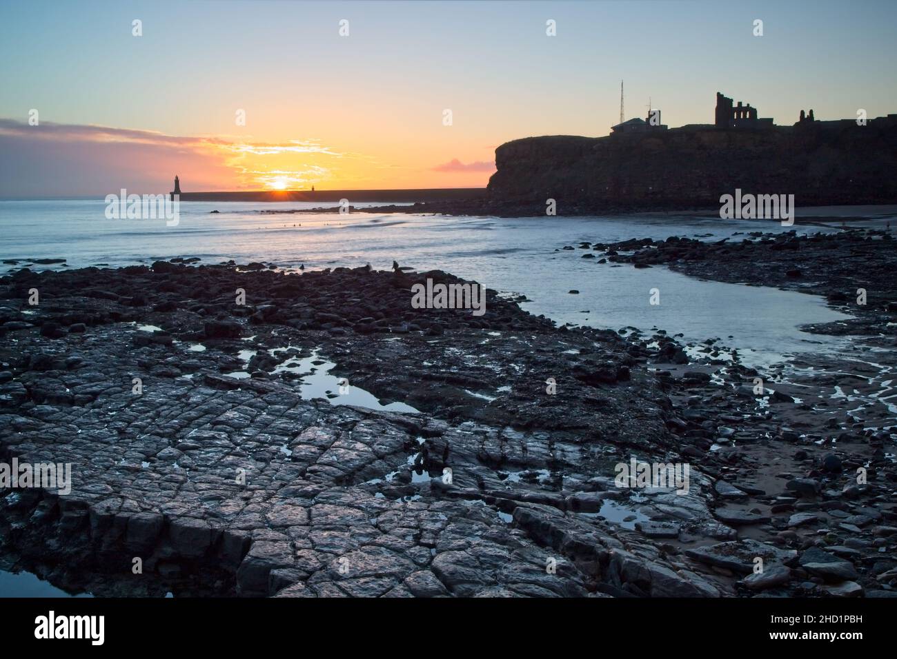 Sunrise at King Edwards Bay, Tynemouth, North Tyneside. The pier and priory are in silhouette in the background while rocks fill the foreground. Stock Photo