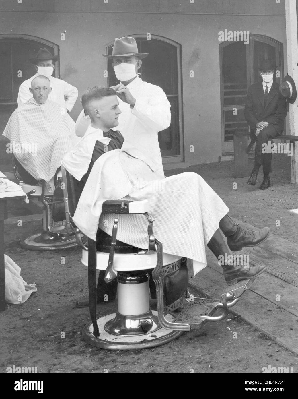 Vintage Photography - Mask wearing during the Spanish Flu pandemic of 1918 - Open air barber shop with customers having their hair cut. Stock Photo