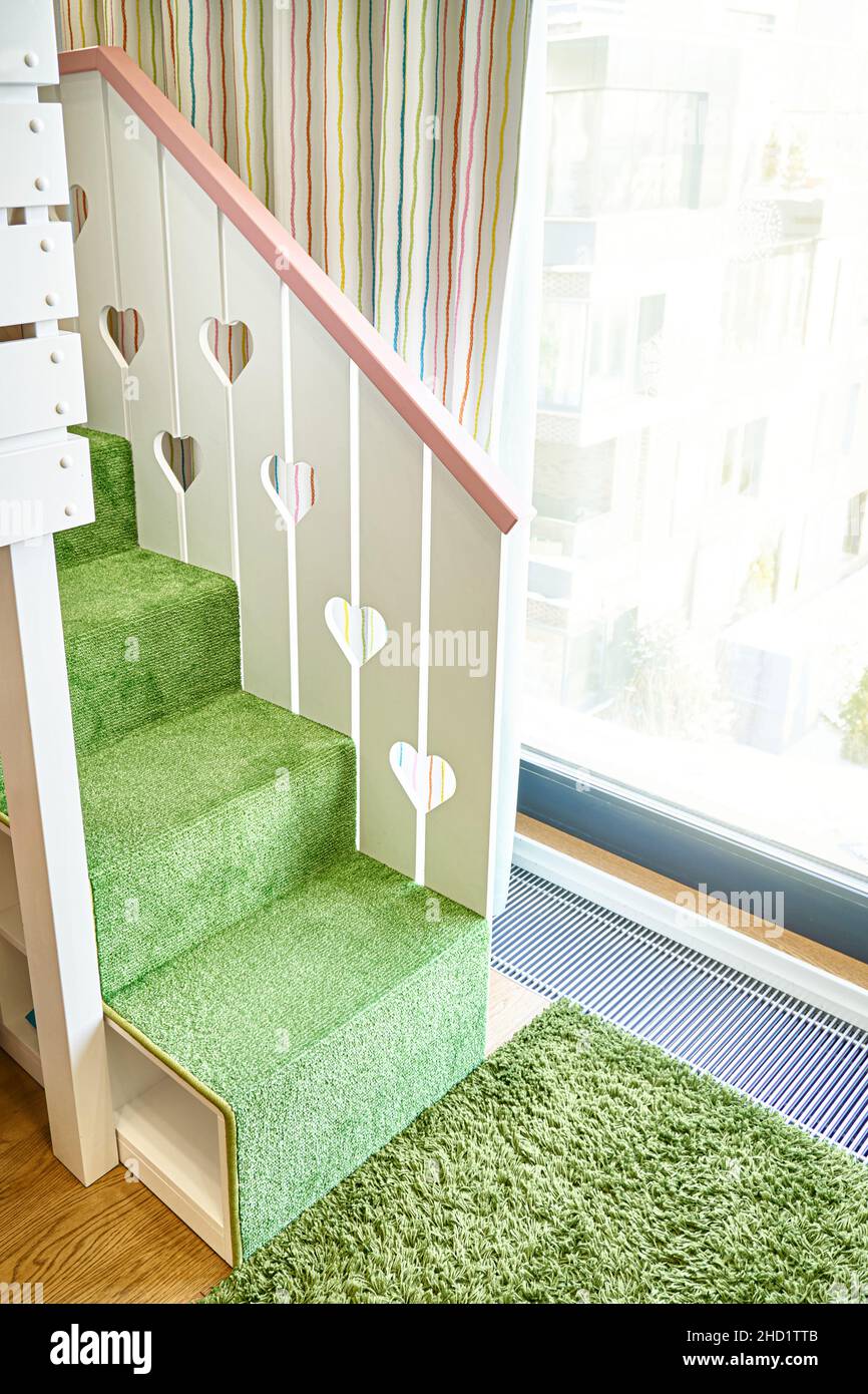 Cute stairs covered with green carpet and wooden handrail with hearts of children playhouse near large window in room closeup Stock Photo