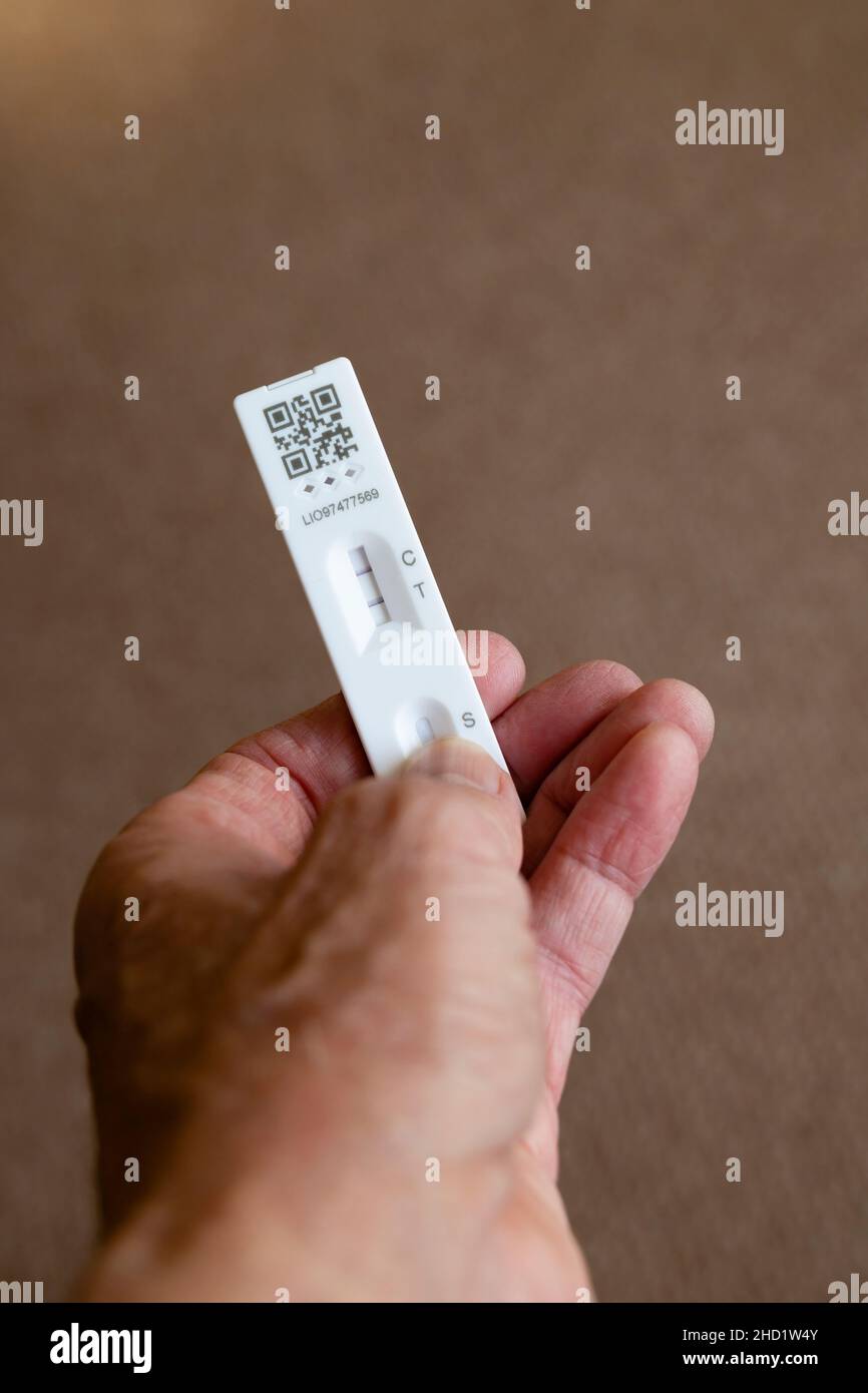 Covid 19 Lateral Flow Test sample showing a positive result in a hand against light brown background. Stock Photo