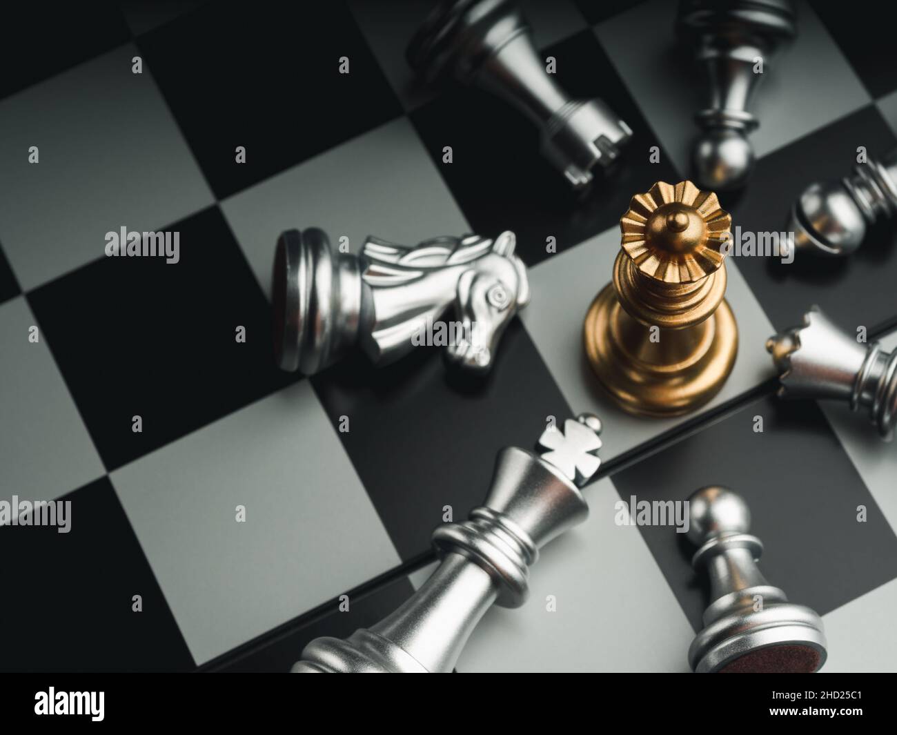 The golden queen chess piece standing with falling silver knight, rook, bishop, pawn pieces on chessboard on dark background, top view. Leadership, wi Stock Photo