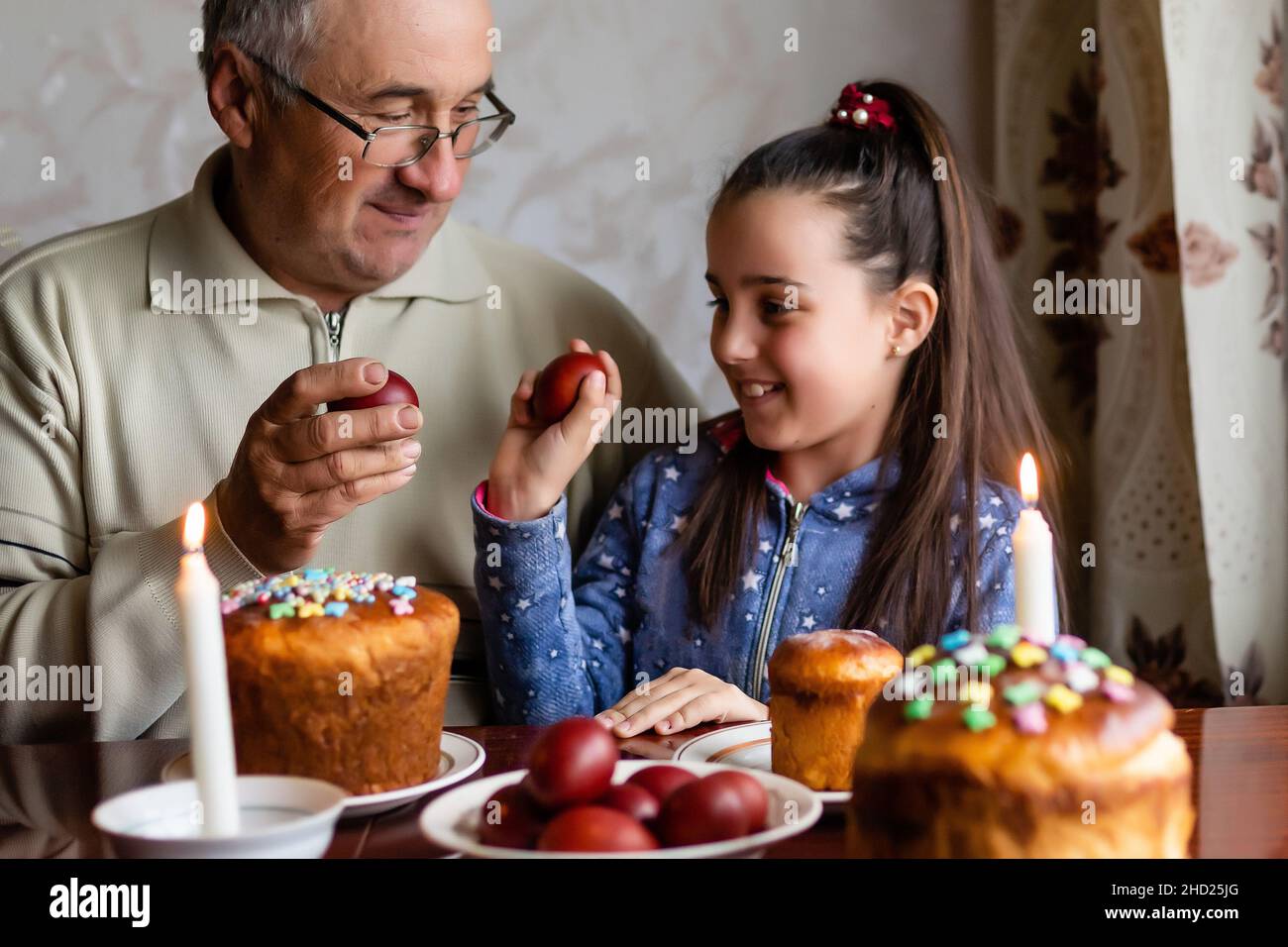 happy grandfather and granddaughter hold easter eggs in hand, folk game