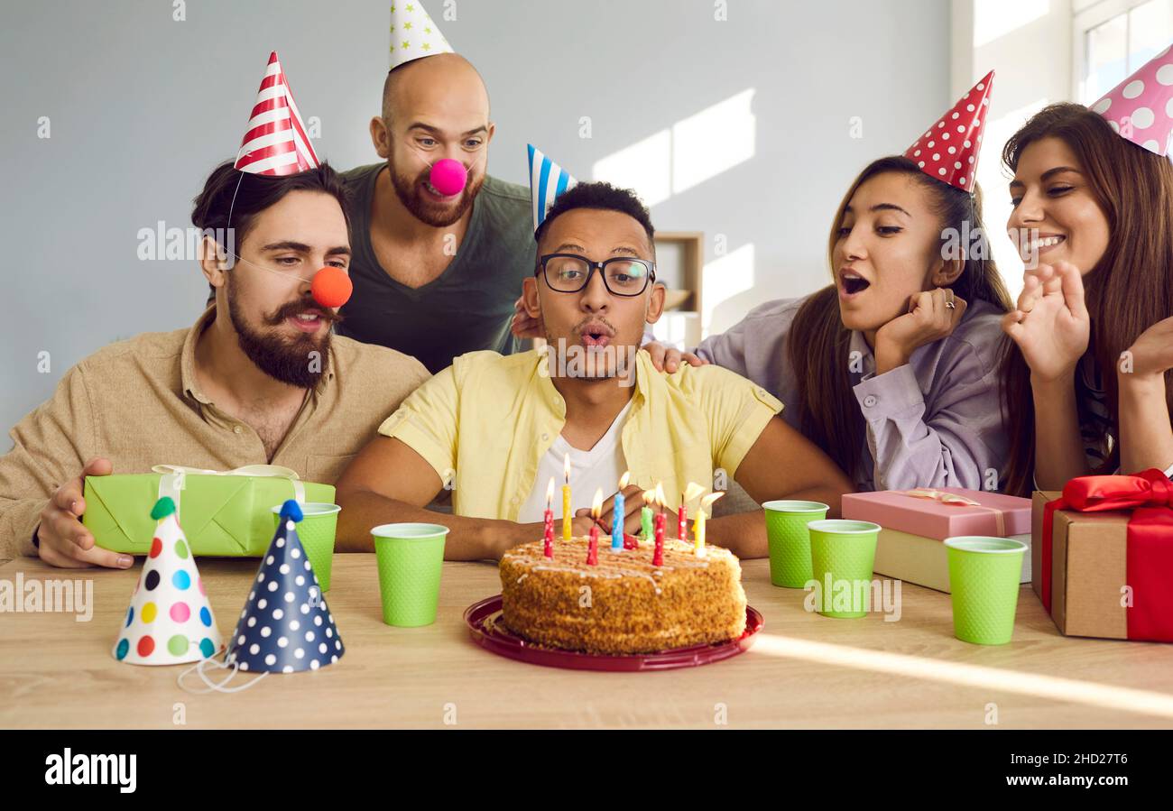 Birthday boy, surrounded by his friends, makes wish and blows out candles on cake. Stock Photo