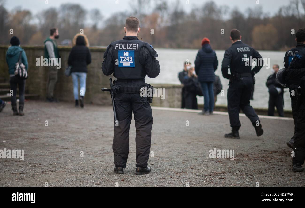 Hanover, Germany. 02nd Jan, 2022. Police officers stand in front of a group of people at the Löwenbastion at the Maschsee. The police of Hanover has unceremoniously assessed a so-called 'Corona walk' - an unregistered event with several people as a protest against the state Corona measures - as an unregistered demonstration. In Hanover, several such gatherings had already been broken up over the weekend - partly too many people were walking together, partly the participants were not wearing masks. Credit: Julian Stratenschulte/dpa/Alamy Live News Stock Photo