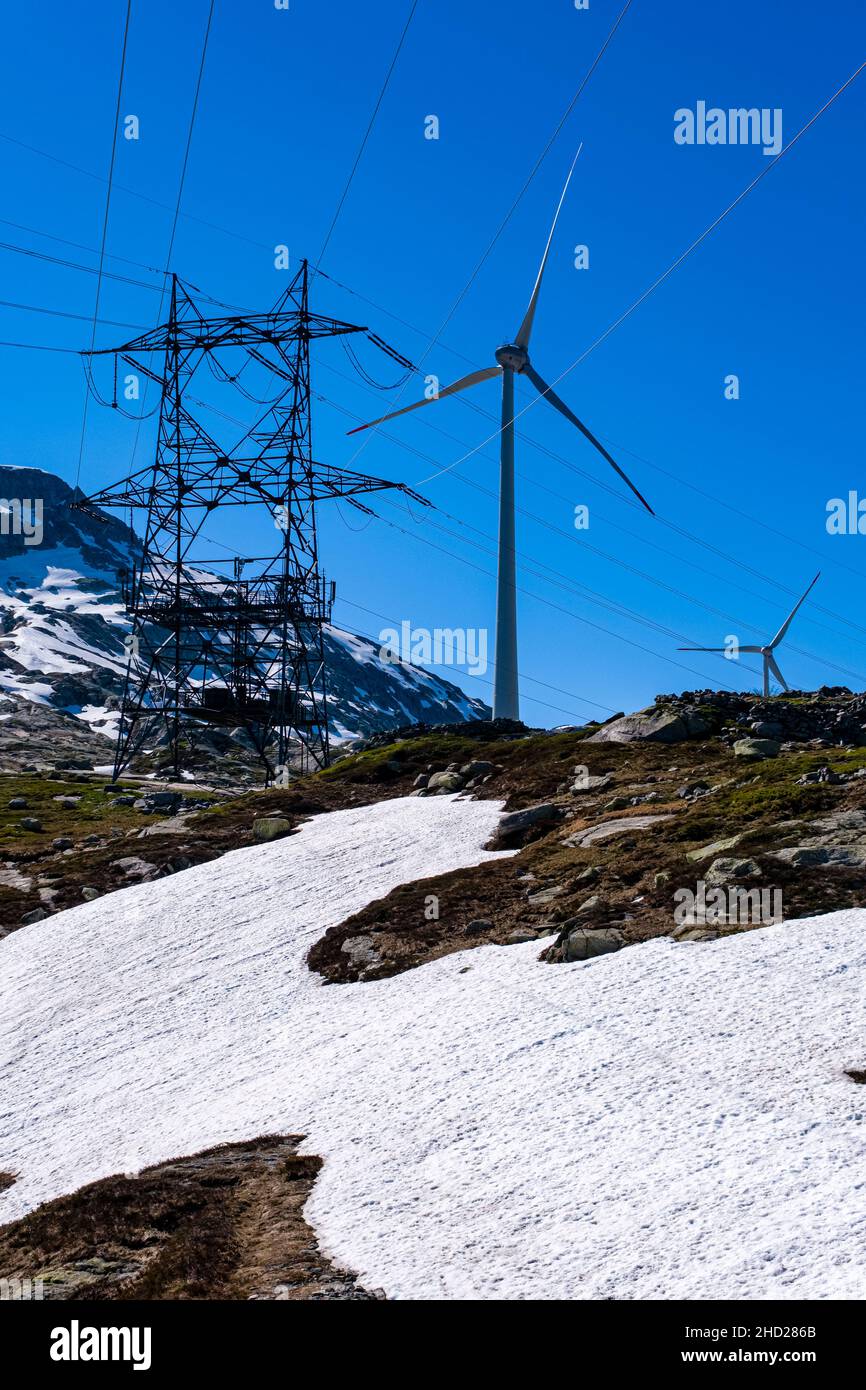 Wind turbines and a high voltage pole on top of Gotthard Pass at 2106 m, surrounding mountains covered in snow. Stock Photo