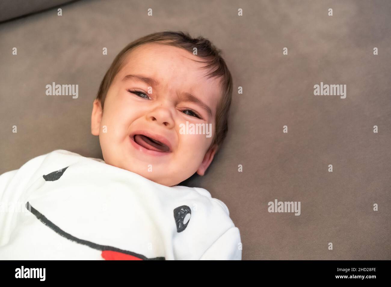 Baby crying with the pain of his first teeth, lying on the sofa at home