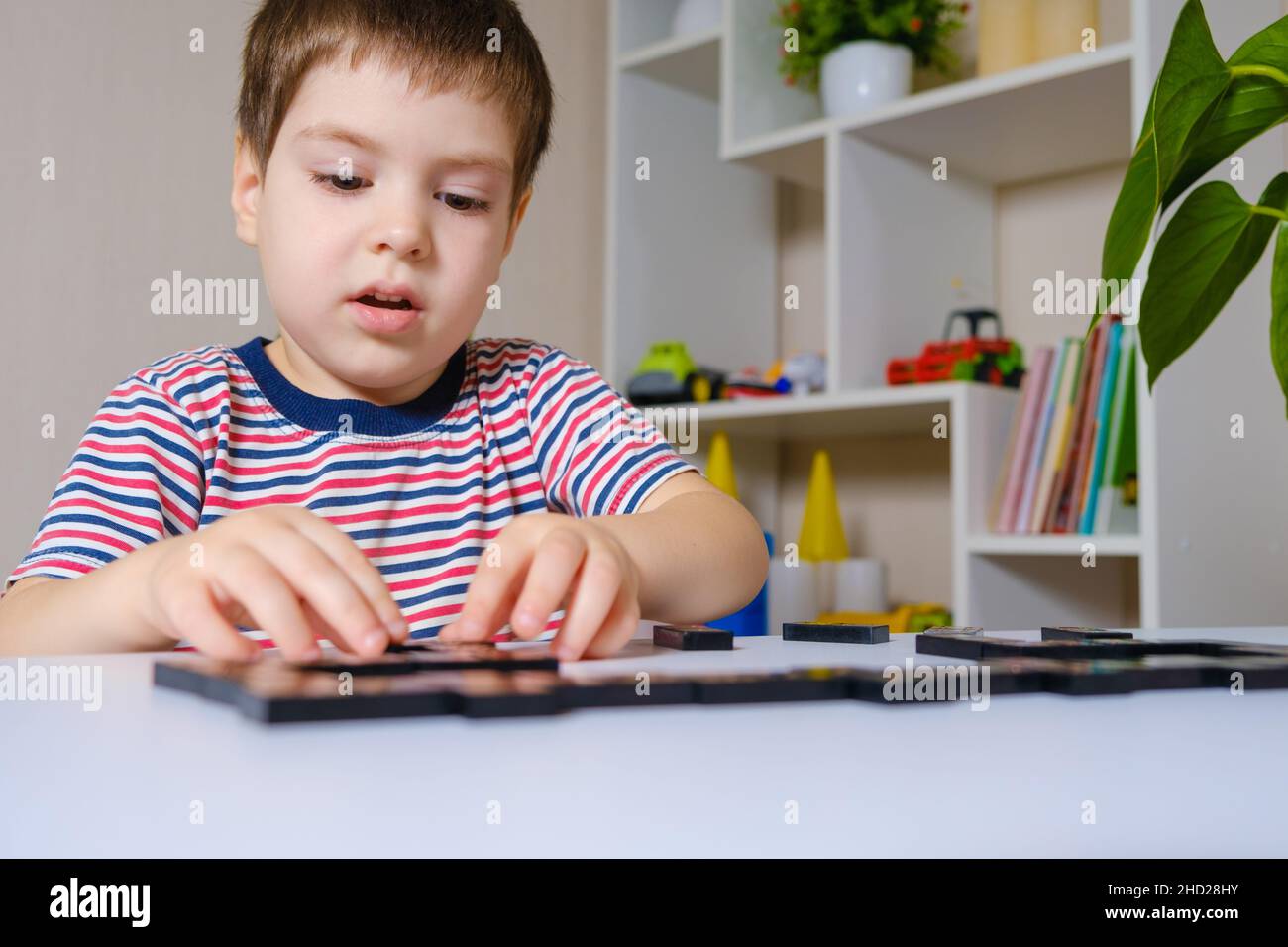 A child in a striped Tshirt plays dominoes. Development and board