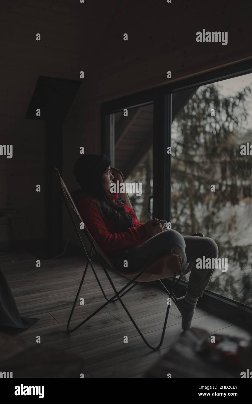 Vertical shot of a Hispanic woman watching a scenic natural view from inside her cottage Stock Photo