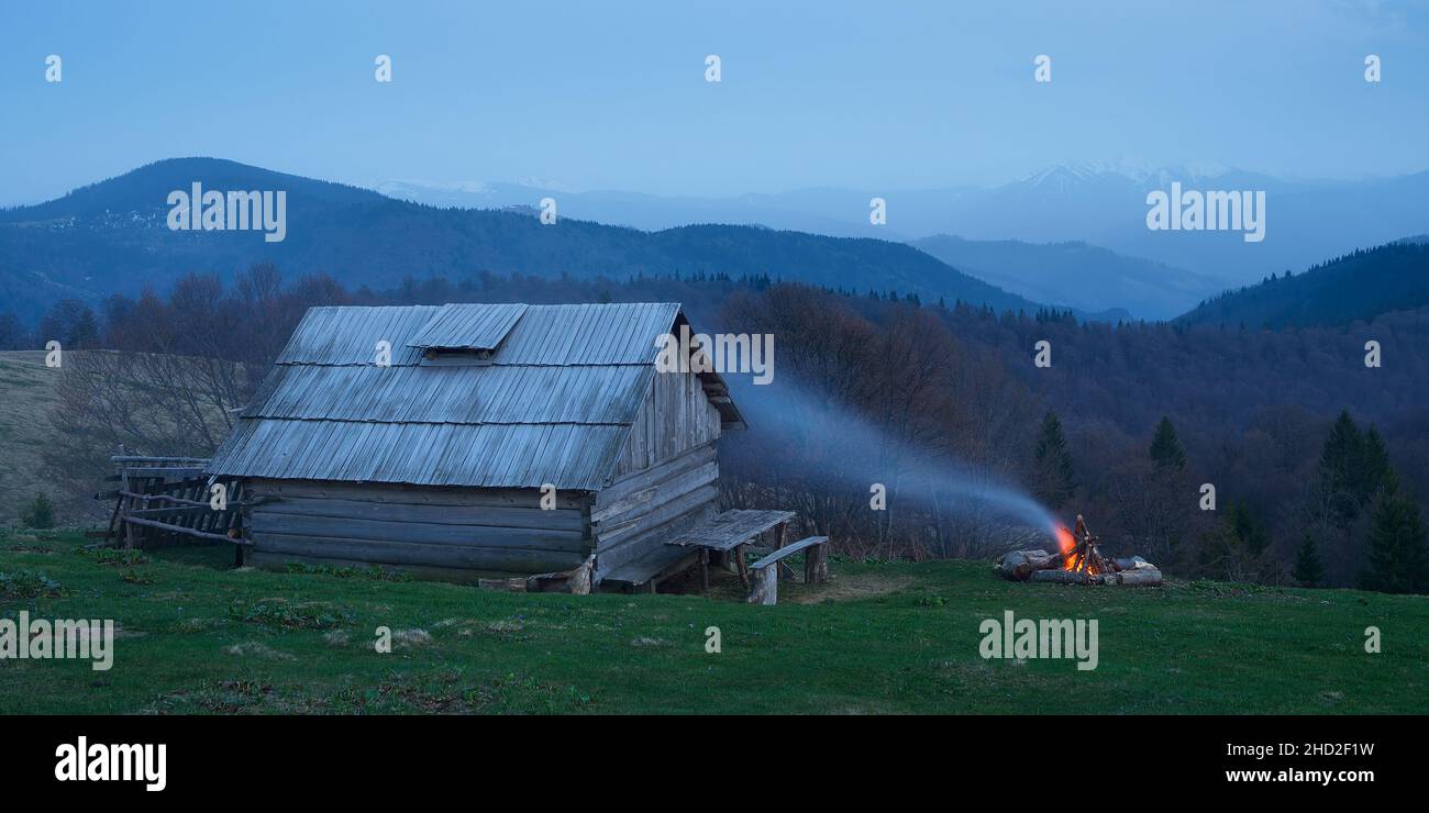 Evening landscape with wooden house and the fire. Camping in the mountains. Twilight after sunset. Carpathian mountains, Ukraine, Europe Stock Photo