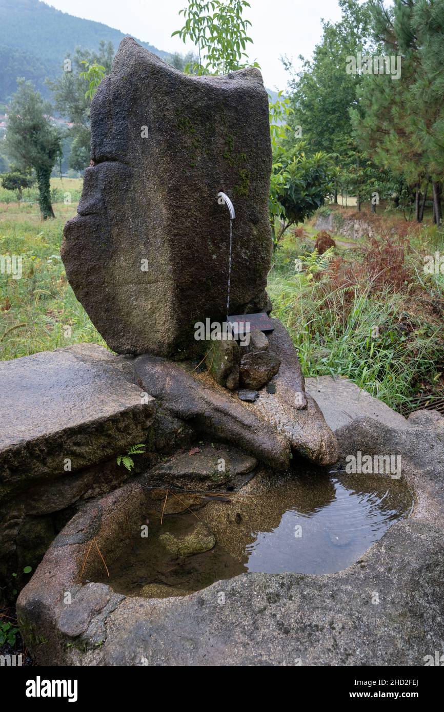 A rustic stone water fountain marked with a warning sign “água não controlada” along the Camino Portuguese in Vitorino dos Piães, Portugal. This route Stock Photo