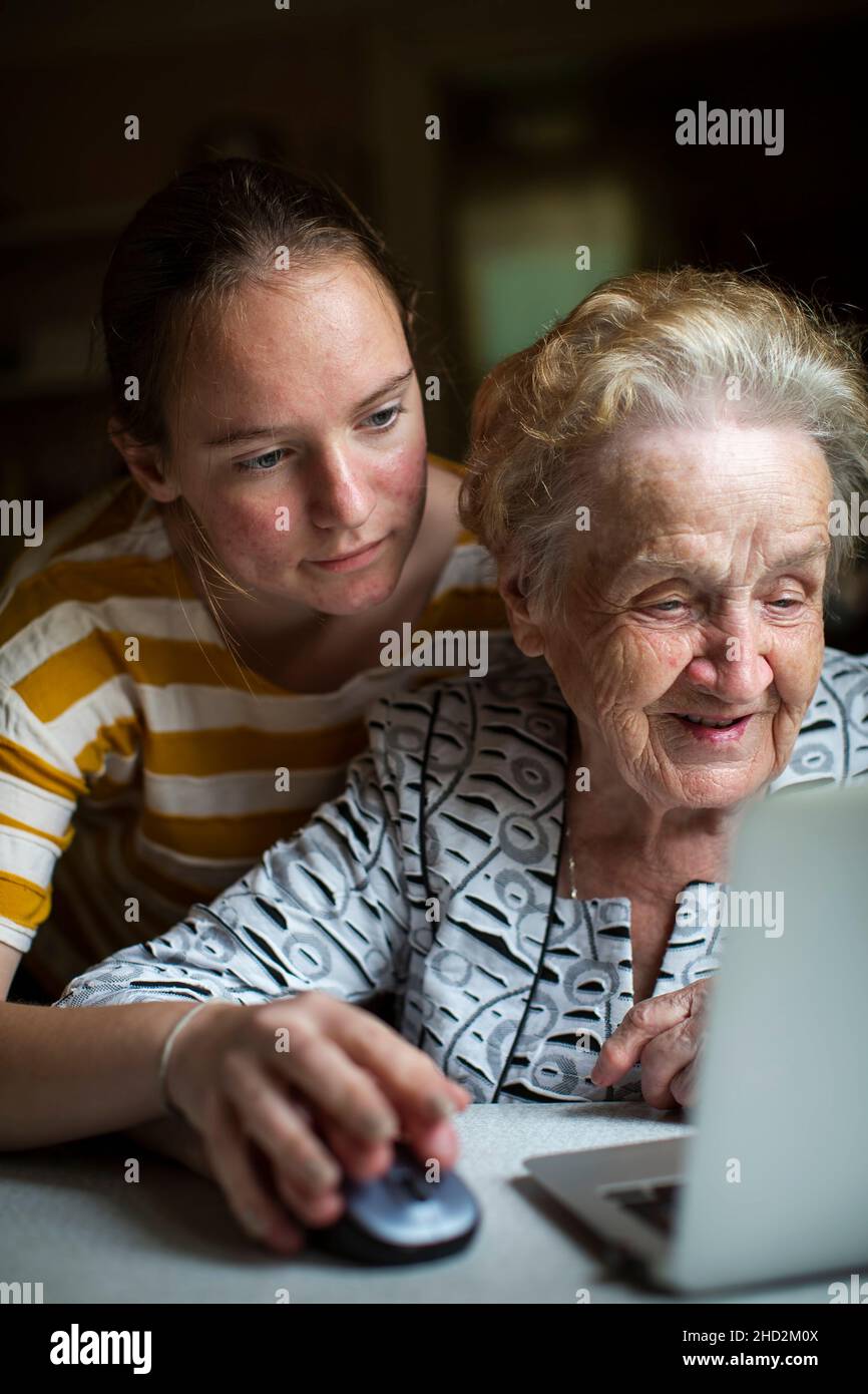 A girl teaches her grandmother how to work a laptop. Stock Photo