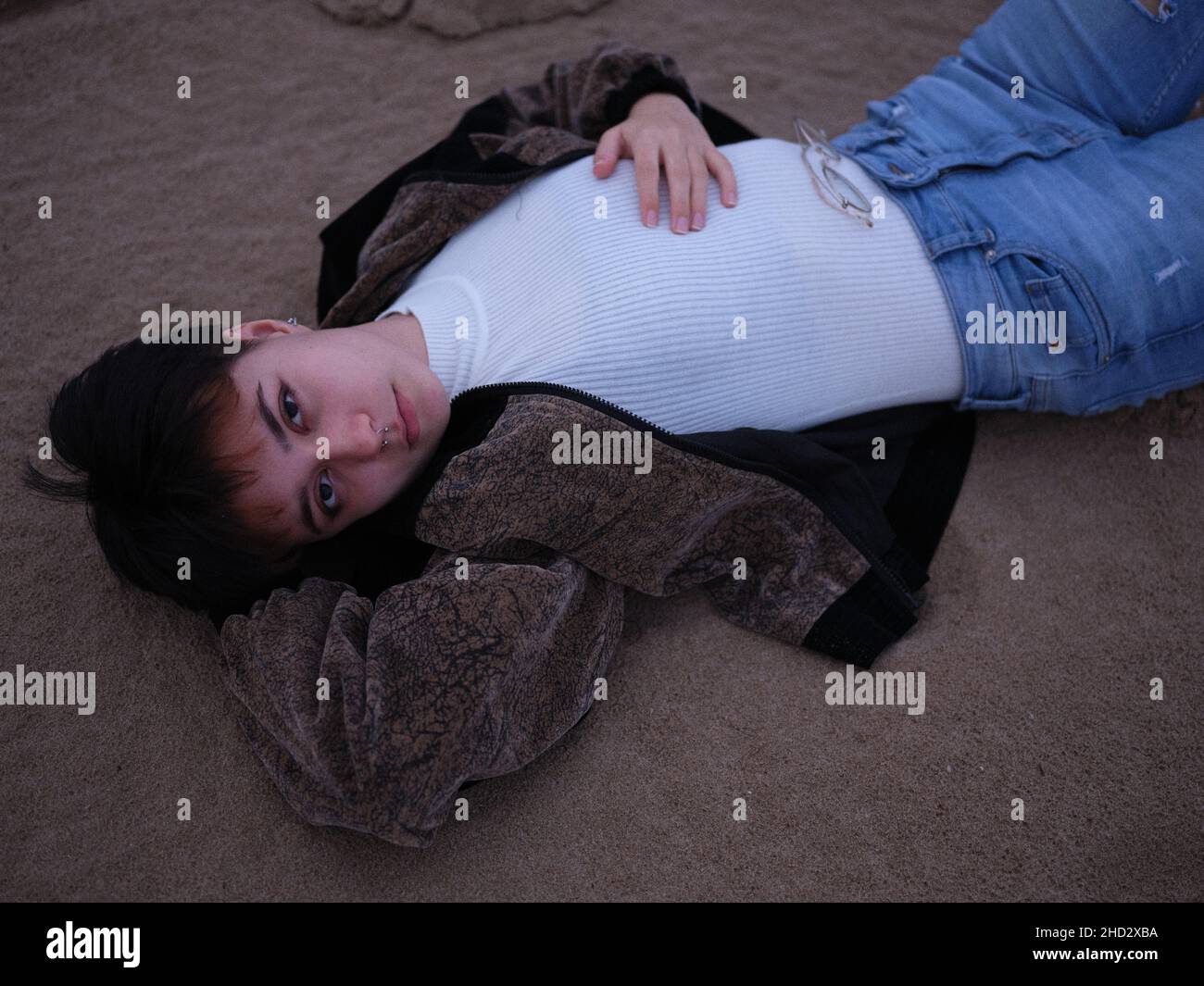 horizontal portrait of a trans girl lying on the beach in warm clothes Stock Photo