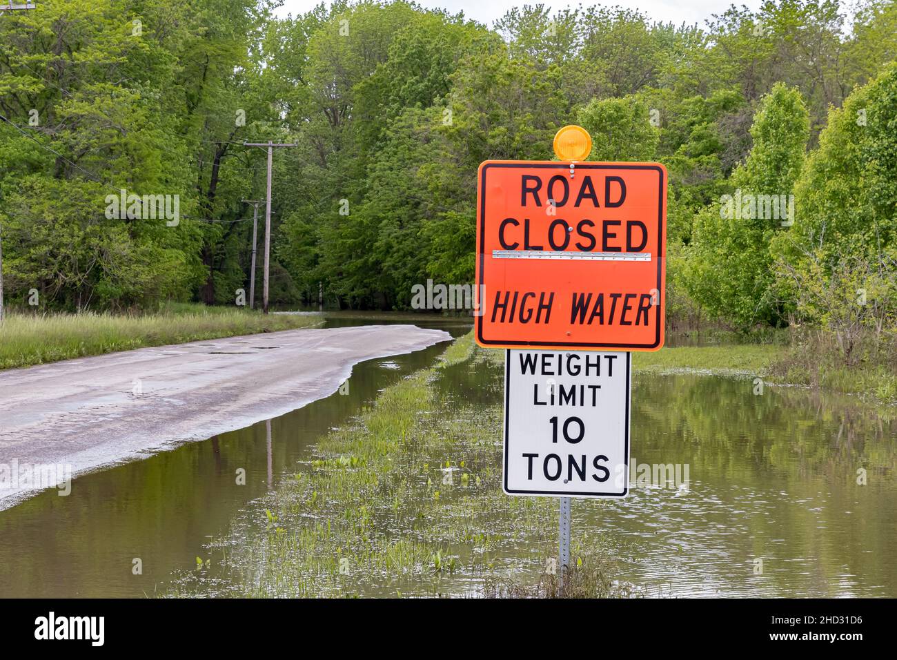 Road closed sign and high water flooding roadway. Storm and rain damage, weather warning and climate change concept. Stock Photo