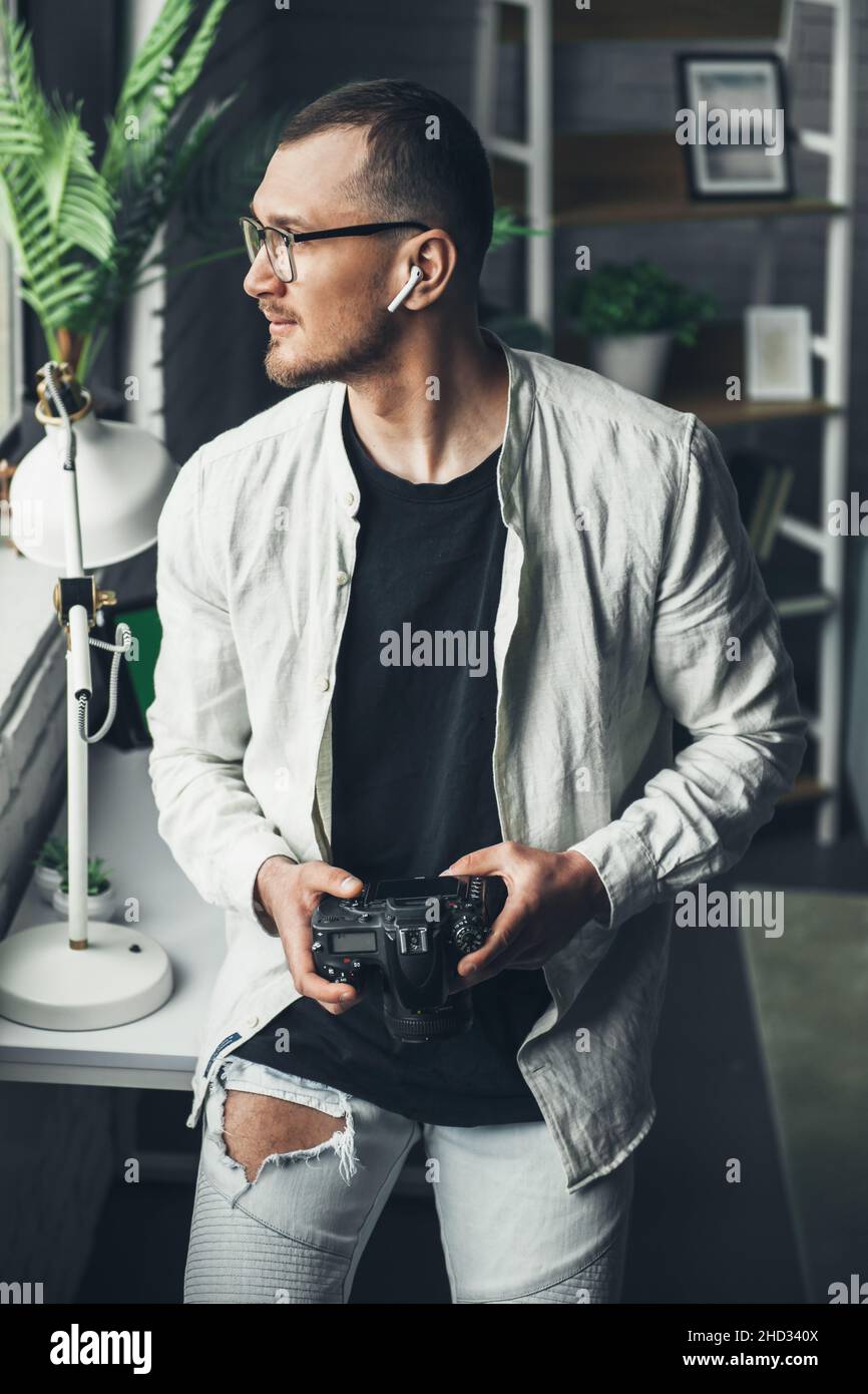 Photograper sitting in studio holding professional photocamera, looking away. Professional work job occupation. Digital art. Stock Photo