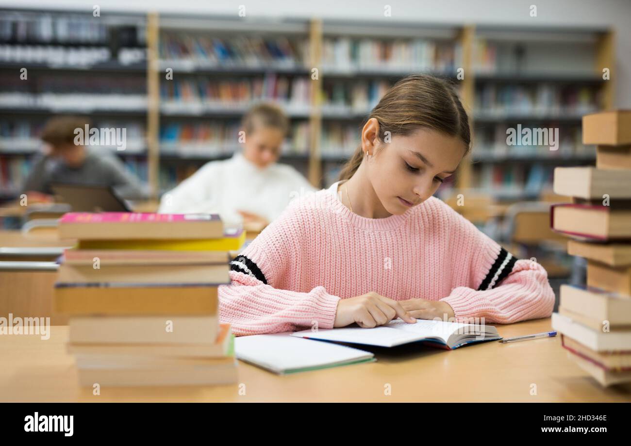 Portrait of preteen girl reading books in college library Stock Photo ...