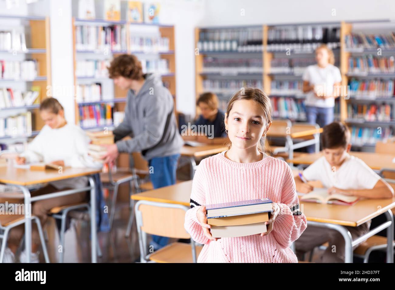Preteen girl standing with a stack of books inlibrary Stock Photo - Alamy