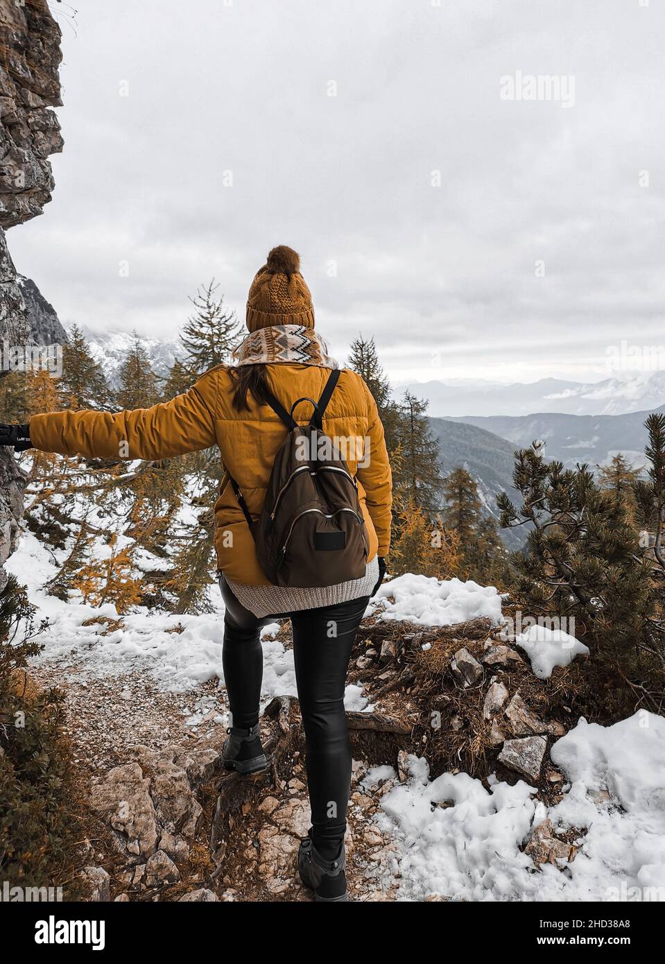 Back view of a Caucasian female hiker on snowy path in mountains in the ...