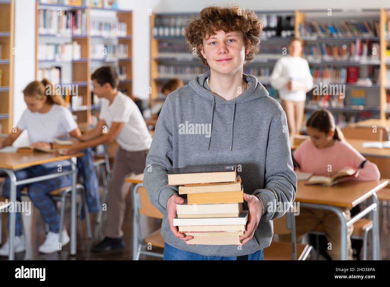 Boy with pile of books in library Stock Photo - Alamy