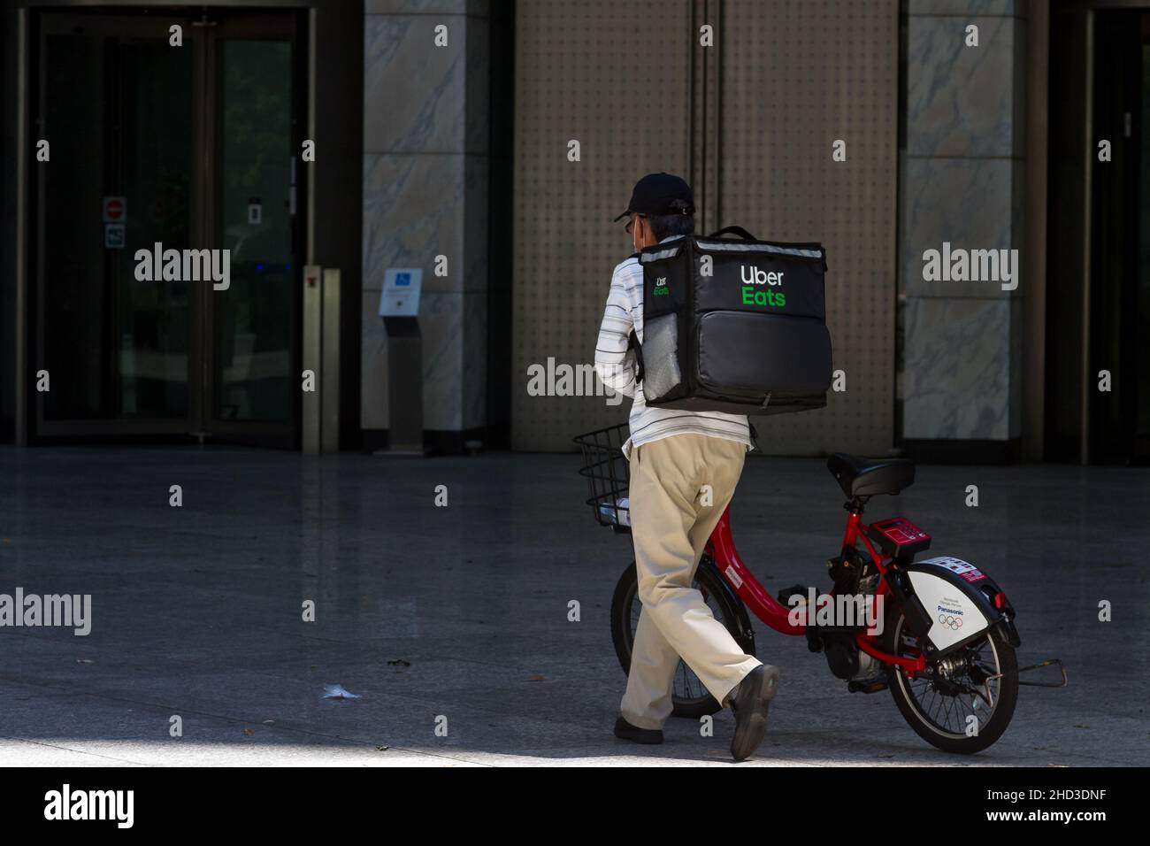 An older Japanese man uses a rental bicycle to deliver food with Uber Eats. Nagatacho,,Tokyo, Japan. Stock Photo