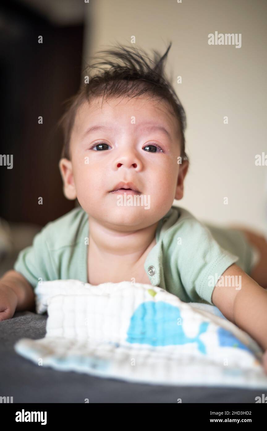 Adorable 2 months old mixed race newborn baby boy lying on his tummy on the bed lifting head and playing Stock Photo